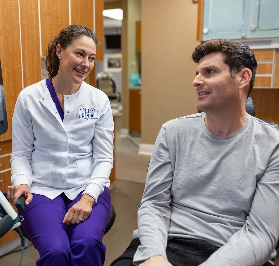Female dentist in white coat consulting male patient in dental office with warm, friendly expressions.