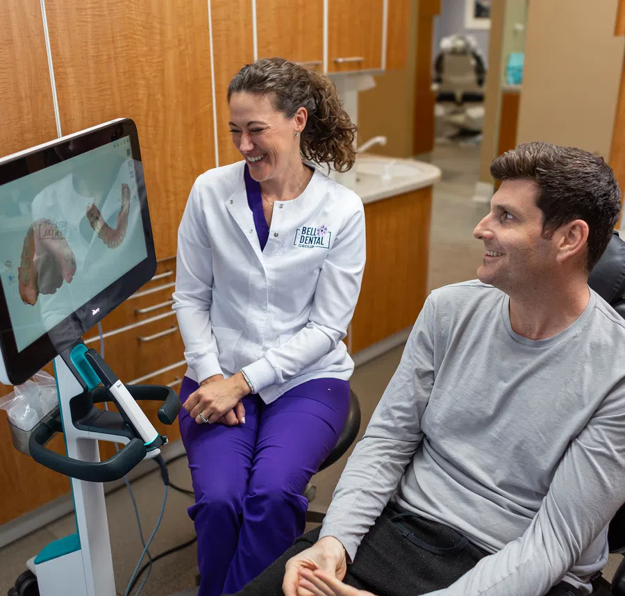 Dentist in white coat smiling with male patient while reviewing dental scan on screen in clinic