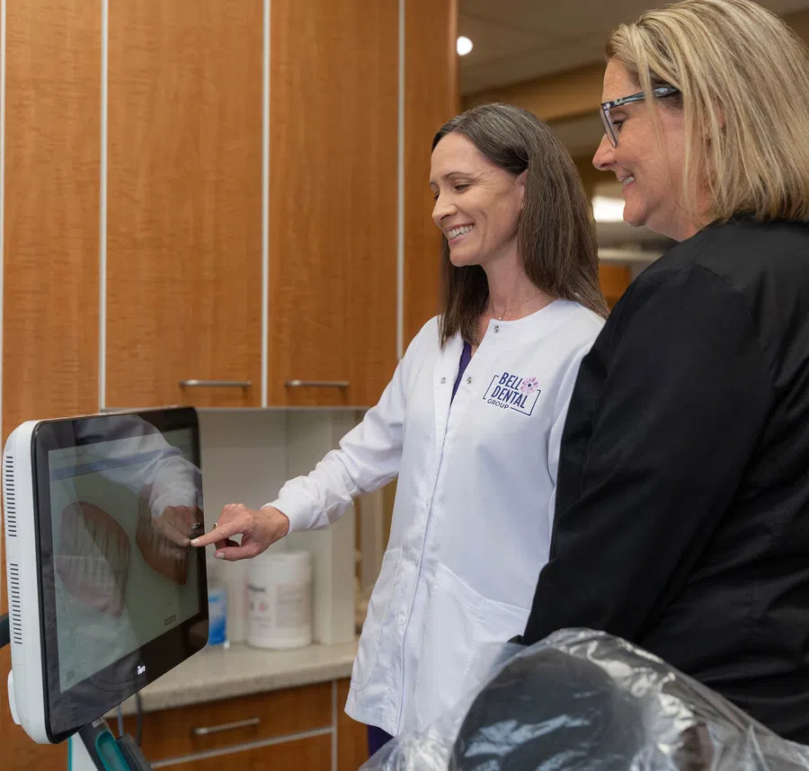 Dental professional explaining digital dental images on a screen to a smiling patient in a clinic.