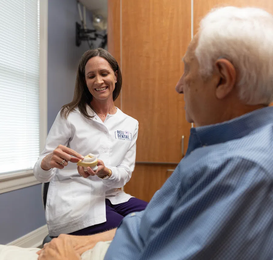 Female dentist explaining dental model to elderly male patient in dental office consultation.