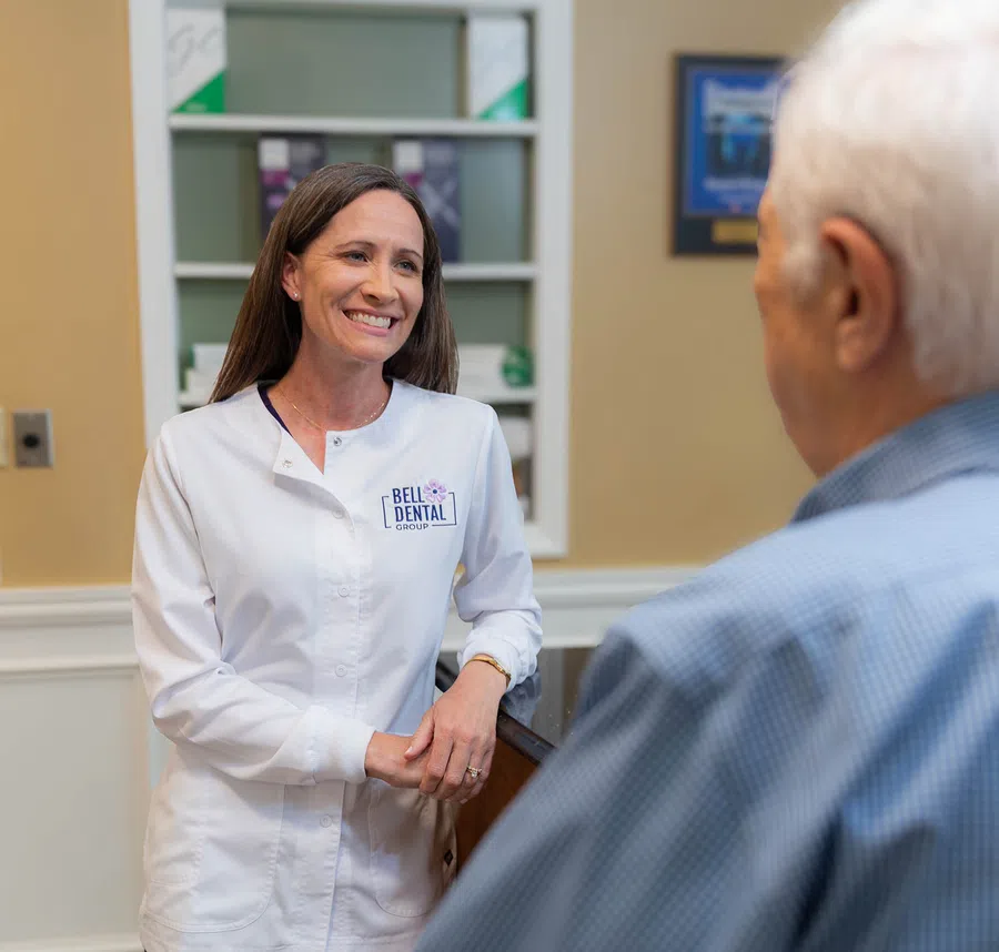 Female dental professional smiling and talking with an elderly male patient inside a dental office.