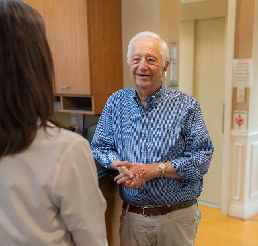 Elderly man in blue shirt smiling and talking to a woman in a medical office reception area.
