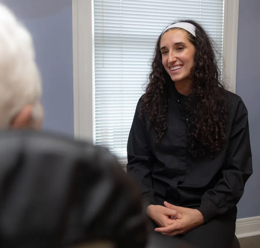 Smiling woman with curly hair and a white headband having a conversation indoors with a blurred person in foreground