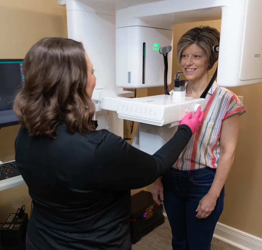 Woman undergoing dental 3D X-ray scan while technician operates the machine in a clinic.