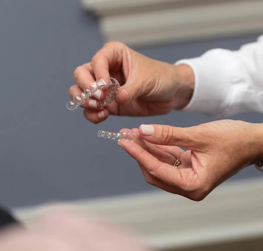 Hands holding clear dental aligners for teeth straightening against a blurred background.