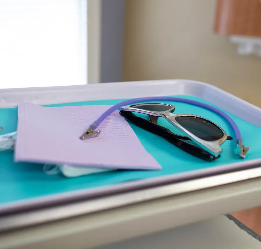 Protective dental eyewear and purple bib placed on a blue tray ready for patient use in a dental clinic.