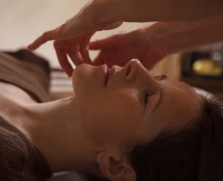 Side view of a woman with closed eyes receiving a relaxing facial massage in a calm setting.