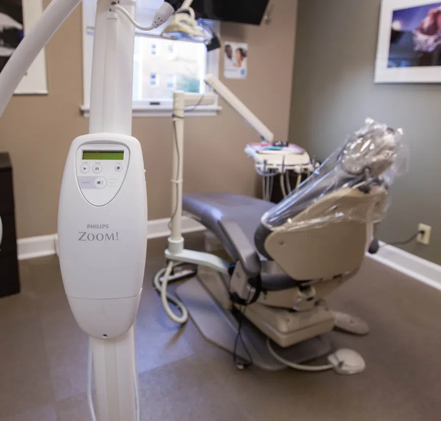 Dental office with Philips Zoom whitening device and patient chair covered in plastic wrap for hygiene.