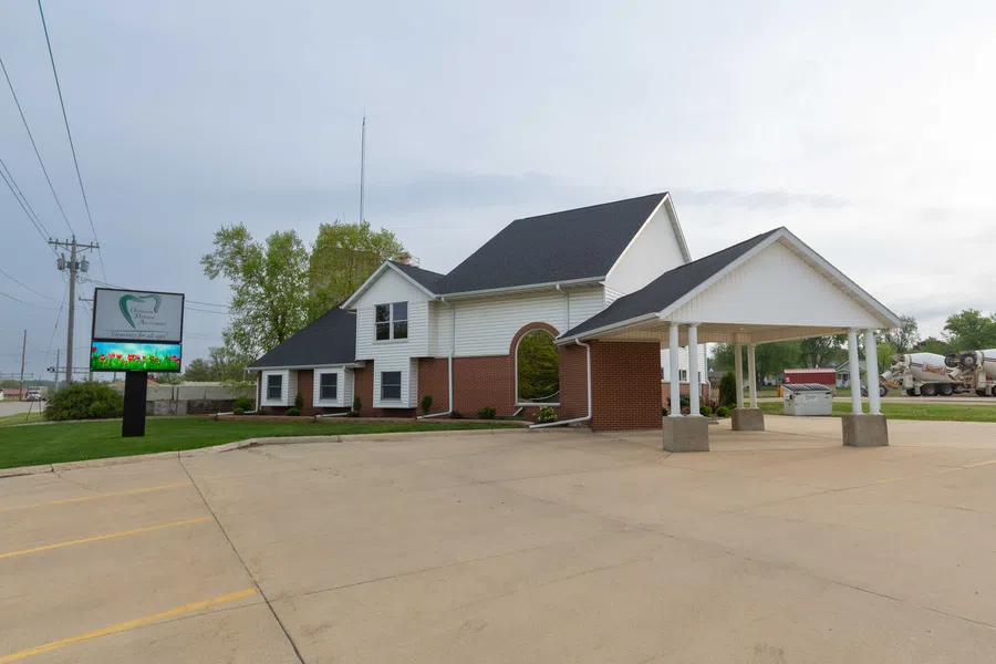 A modern dental office building with white siding, brick accents, and a covered entrance under a cloudy sky.