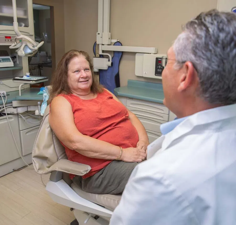 Smiling middle-aged woman talking to male dentist in dental clinic chair during consultation.