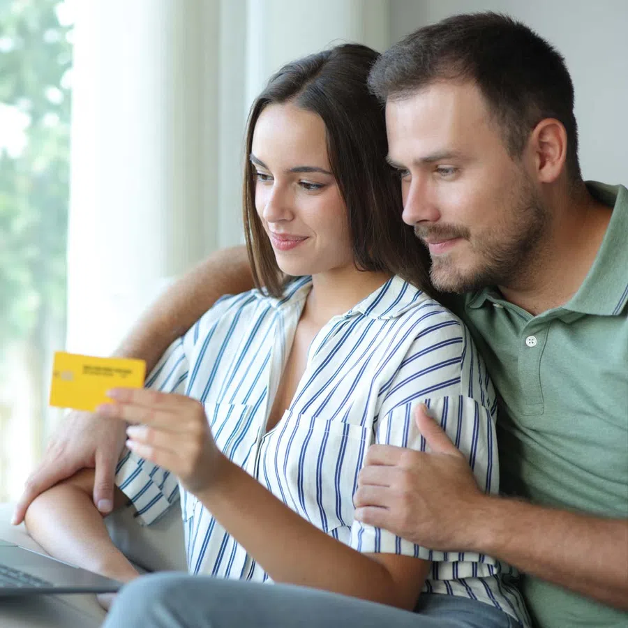 Couple shopping online at home with credit card and laptop, smiling and focused on screen.