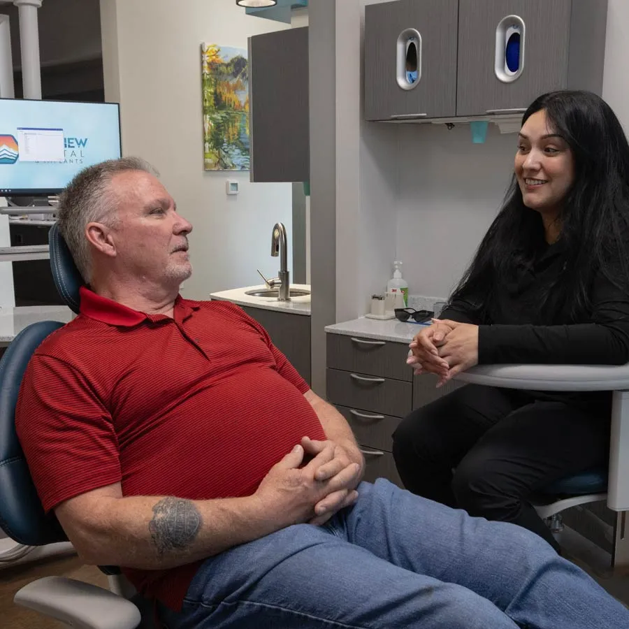 Middle-aged man in red shirt sitting in dental chair talking with female dentist in modern dental office