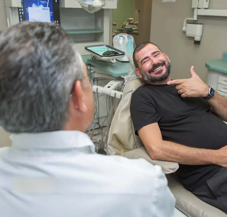 Smiling man pointing to his teeth while sitting in a dental chair during a dentist consultation session.
