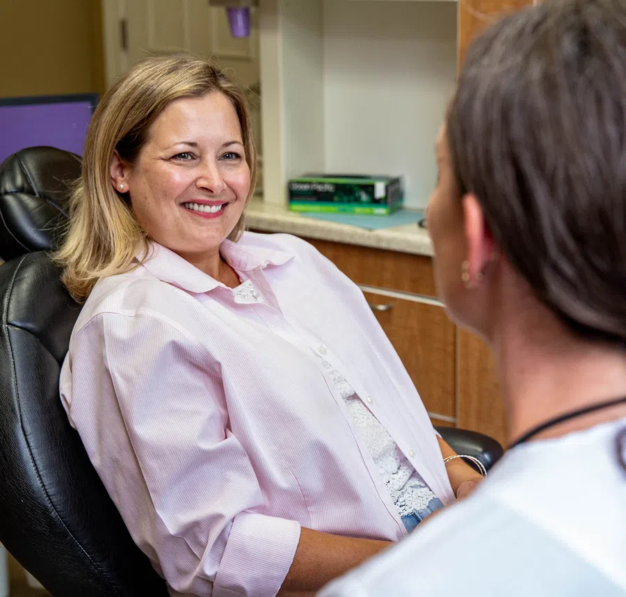 Smiling woman sitting in a dental chair talking to a dental professional in a clinic.