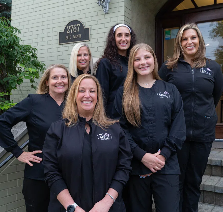 Group of six smiling women dental professionals in black uniforms outside building at 2767 Erie Avenue