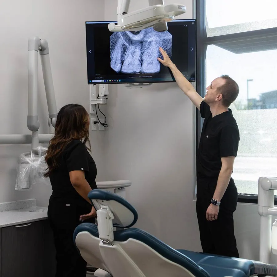 Dentists examining dental X-ray images displayed on a screen in a modern dental clinic room.