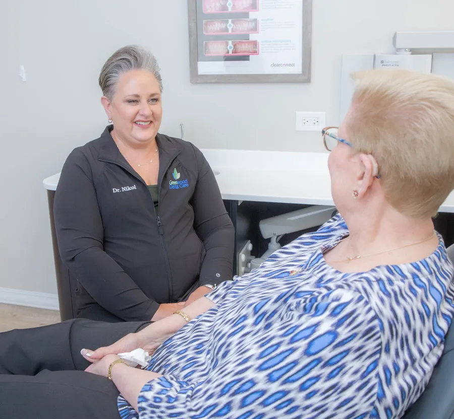 Female doctor in black jacket consulting with senior woman patient in blue patterned blouse in medical office