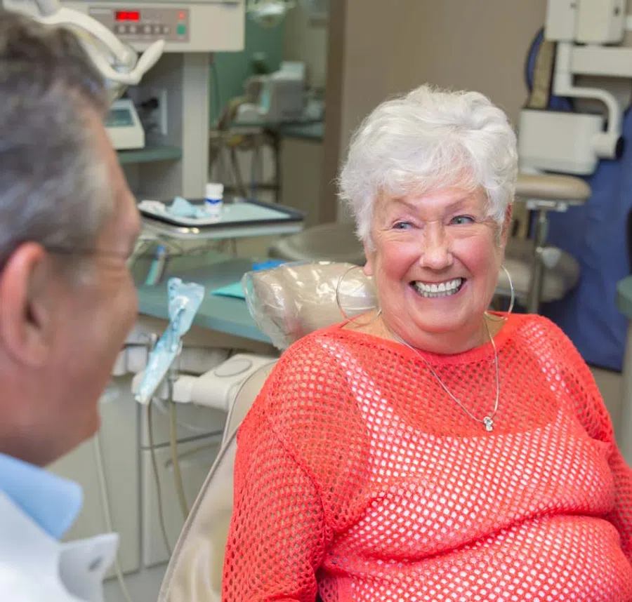 Smiling elderly woman in a dental chair talking to dentist during a checkup in a clinic.