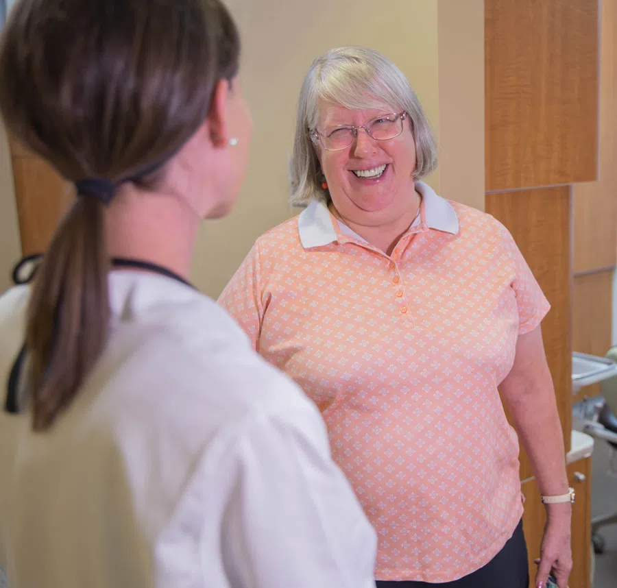 Smiling elderly woman in peach shirt talking to female doctor in clinical setting
