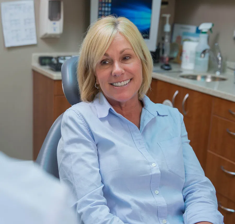 Smiling middle-aged woman in light blue shirt sitting in a dental office chair during a consultation