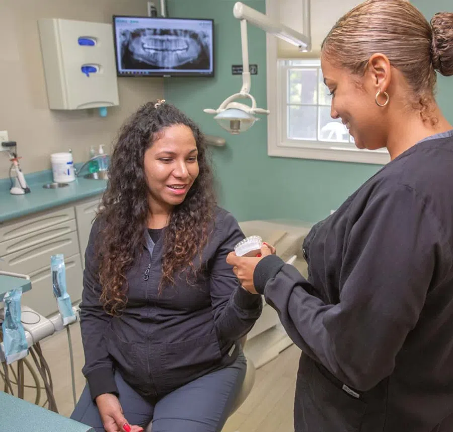 Dentist showing dental mold to patient in clinic with dental X-ray on monitor