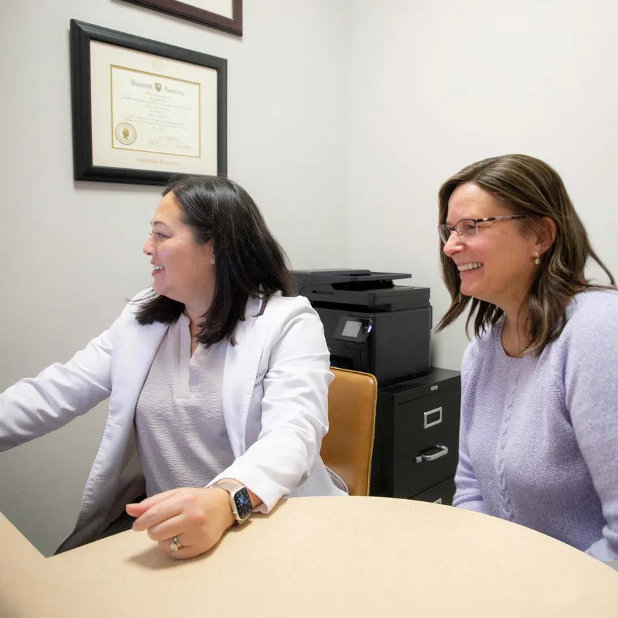Dentist in white coat talking with patient seated in dental chair in a modern clinic room.