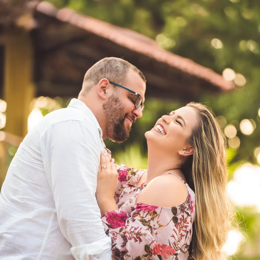 Smiling couple hugging outdoors in a forest with natural light and green trees in the background