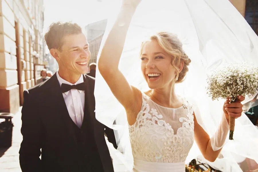 Happy bride and groom smiling outdoors during daytime wedding celebration on a sunny day