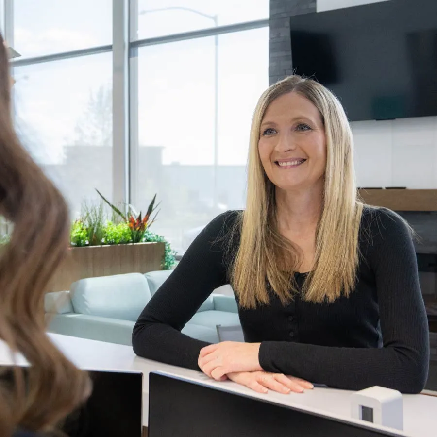 Smiling woman with long blonde hair sitting and talking across a desk in a bright modern office setting