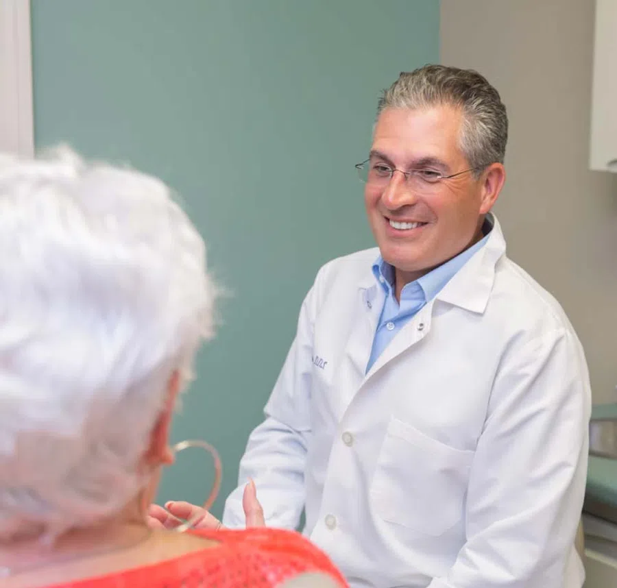 Smiling male doctor consulting an elderly woman in a medical office, showing care and professionalism.