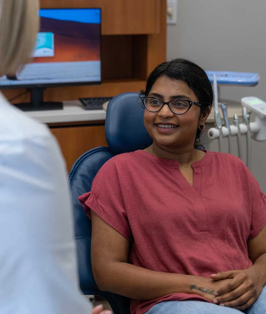 Smiling woman in glasses sitting in a dental chair talking to a dentist in a dental office.