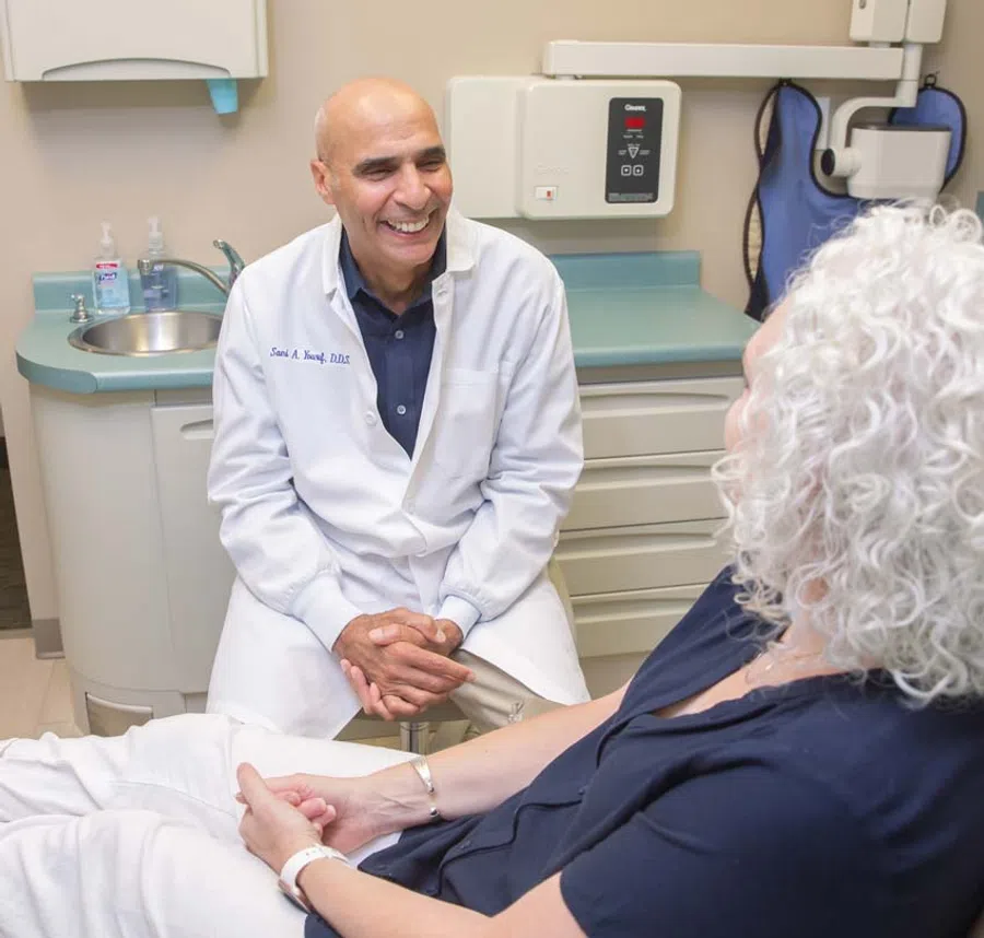 Smiling male dentist in white coat talking with female patient in dental office during consultation