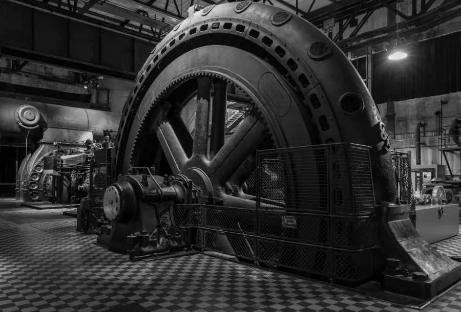 Large vintage industrial machine with massive flywheel inside an old factory with tiled floor