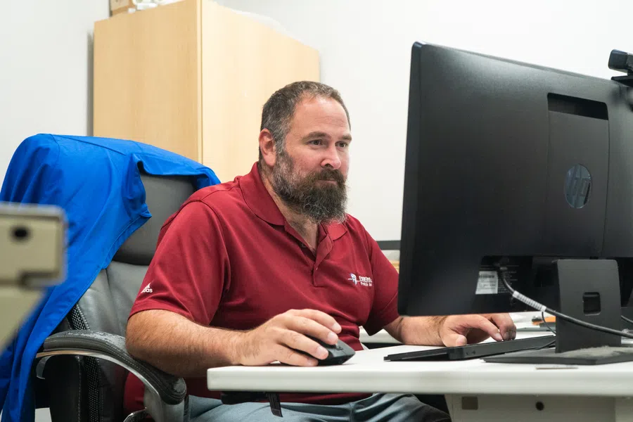 Man in red polo shirt working on desktop computer at office desk with blue jacket on chair