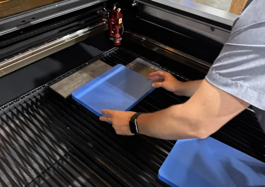 Person placing blue material inside laser cutting machine with red laser head and metal surfaces