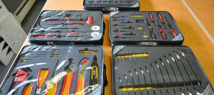 Set of organized tool kits with pliers, screwdrivers, files, and other hand tools in foam-lined cases on a wooden floor