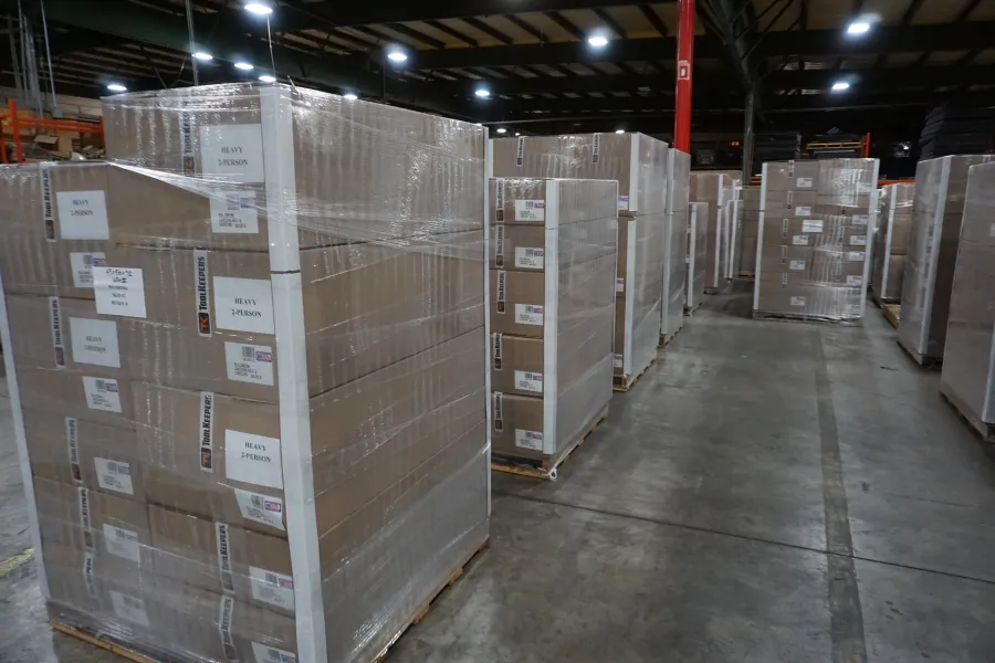 Warehouse with rows of palletized boxes wrapped in plastic on a concrete floor under industrial lighting.
