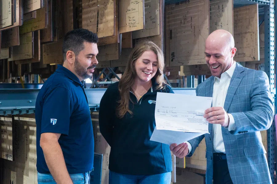 Three coworkers in a warehouse reviewing a document together, smiling and engaged in discussion.