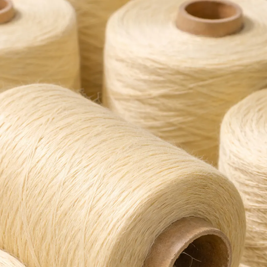 Close-up of natural beige yarn spools tightly wound on cardboard cones, ready for textile production.
