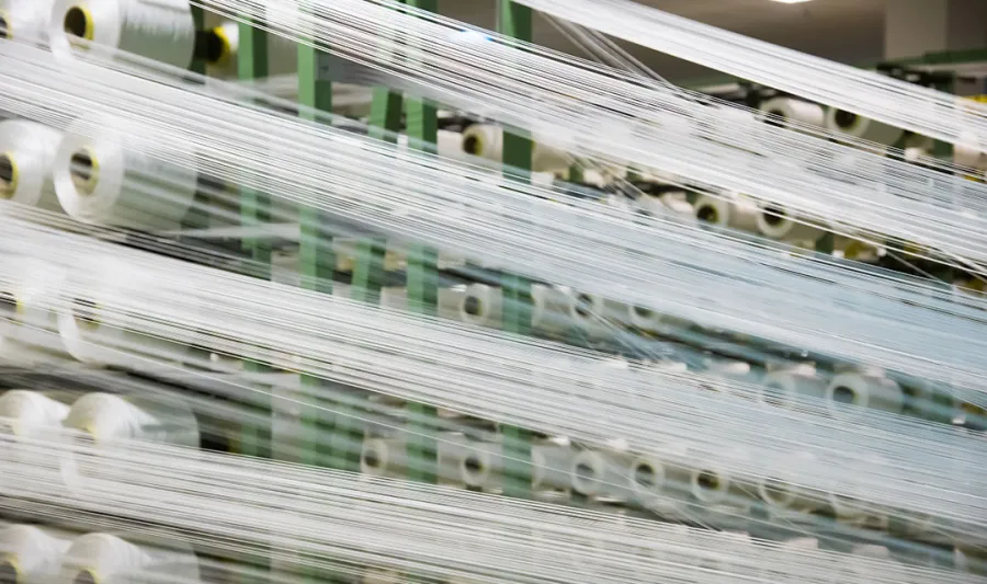 Industrial textile machine with multiple spools of white thread stretched and aligned in a factory setting.