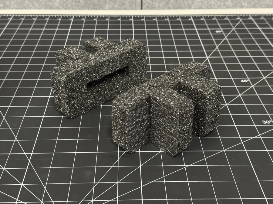 Two black textured foam pieces with rectangular and curved shapes on a black cutting mat with measurement grid.