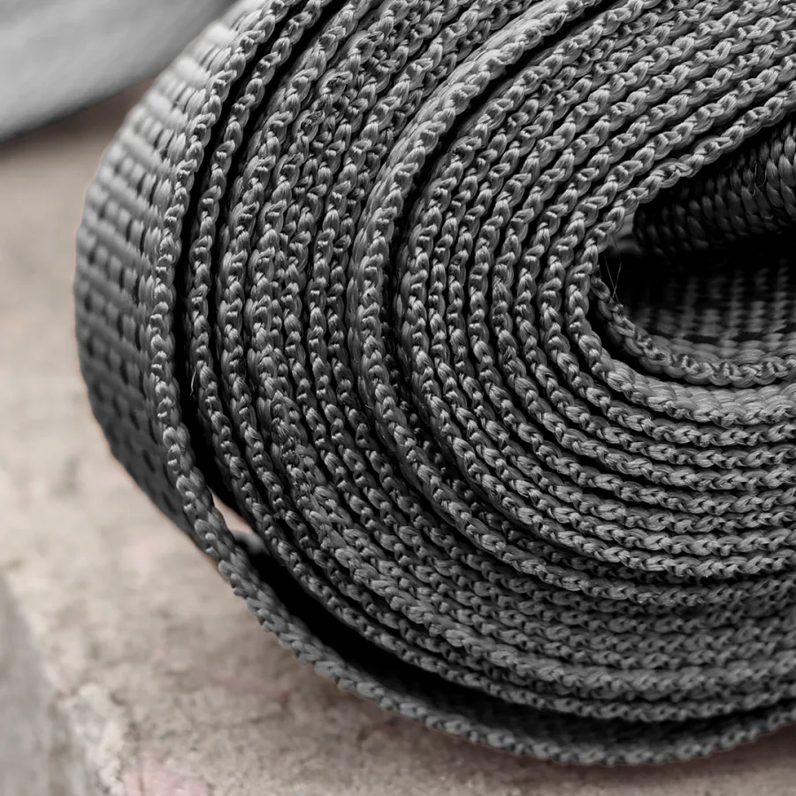 Close-up of tightly coiled black woven strap with detailed braided texture on rough surface.