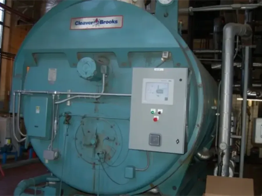 Large blue Cleaver-Brooks industrial boiler with control panel and pipes in a mechanical room.