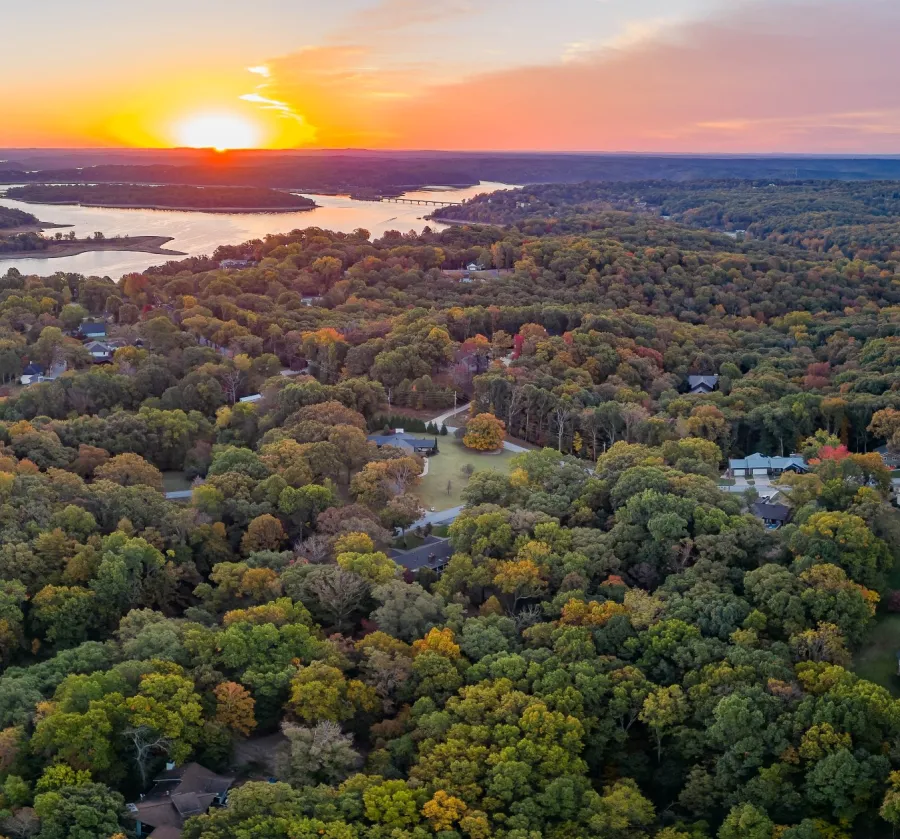 Aerial view of a vibrant landscape at sunset, showcasing trees, water, and a serene atmosphere.