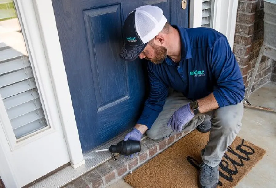 Man installing a product at a blue front door, wearing a cap and gloves, focused on his task.
