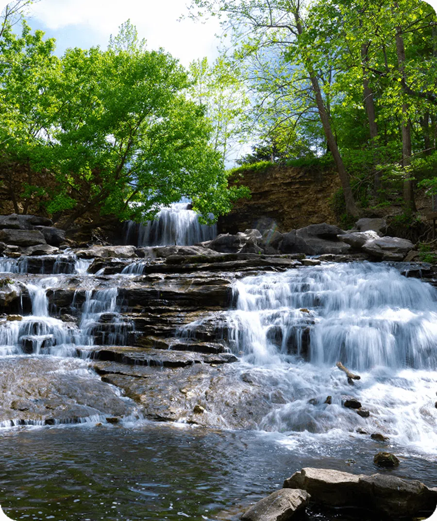Cascading waterfall over rocky tiers surrounded by lush green trees on a bright day