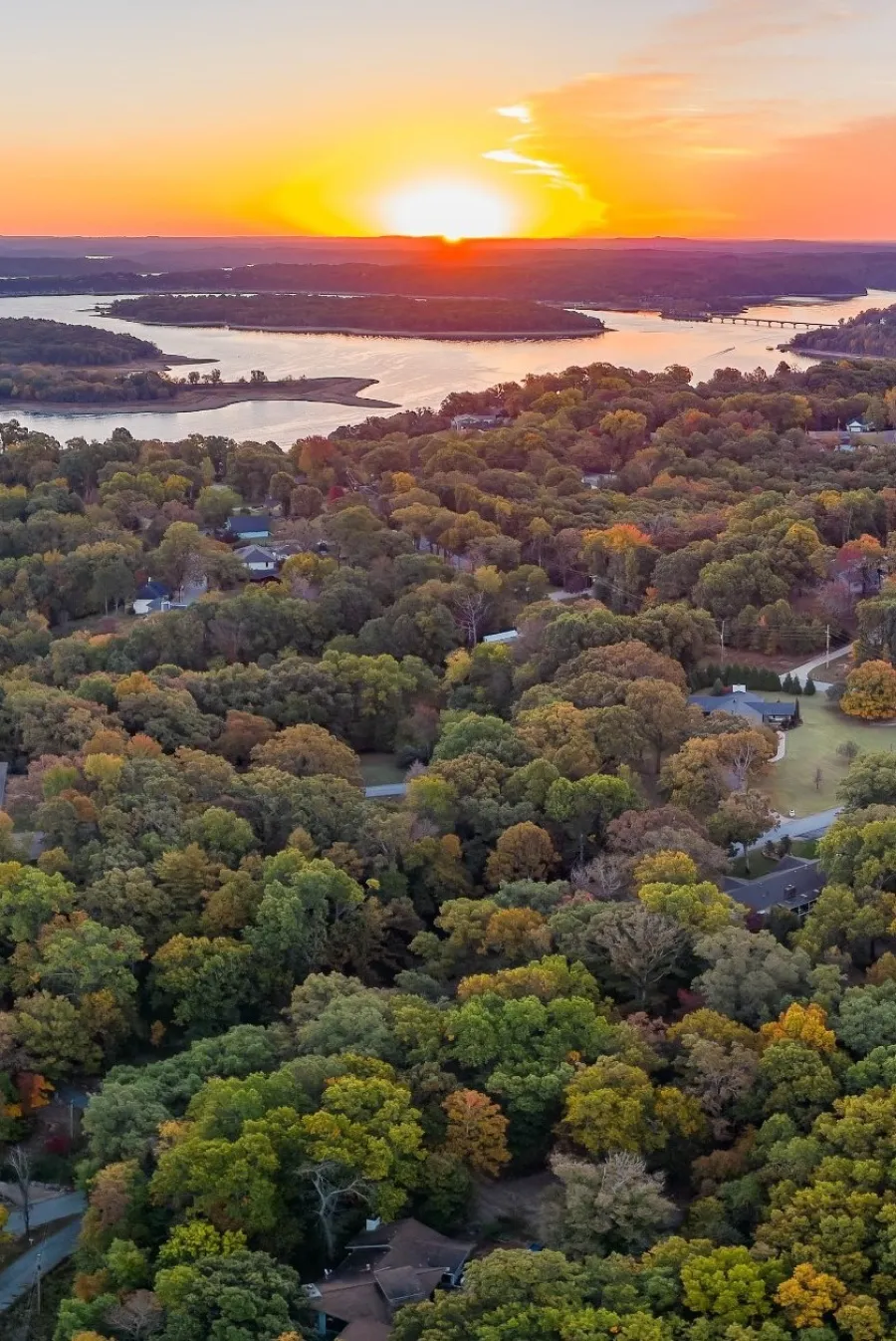 Aerial view of a vibrant autumn landscape at sunset, with a lake and colorful trees.