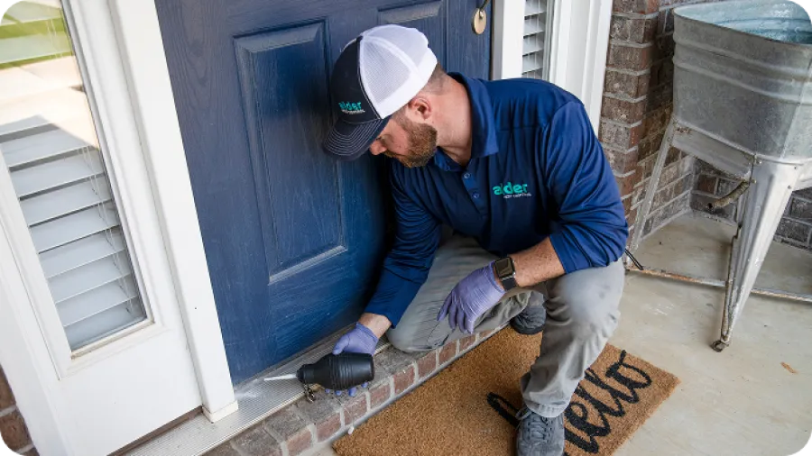 Technician in blue uniform inspecting and sealing the bottom of a blue door on a brick porch.