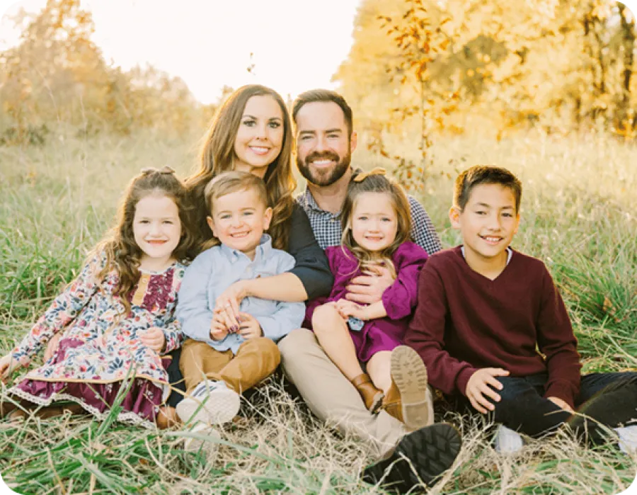 A joyful family poses together in a sunlit field during autumn, surrounded by tall grass.