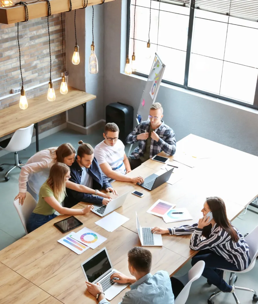 A group collaborating around a wooden table with laptops in a modern office space.